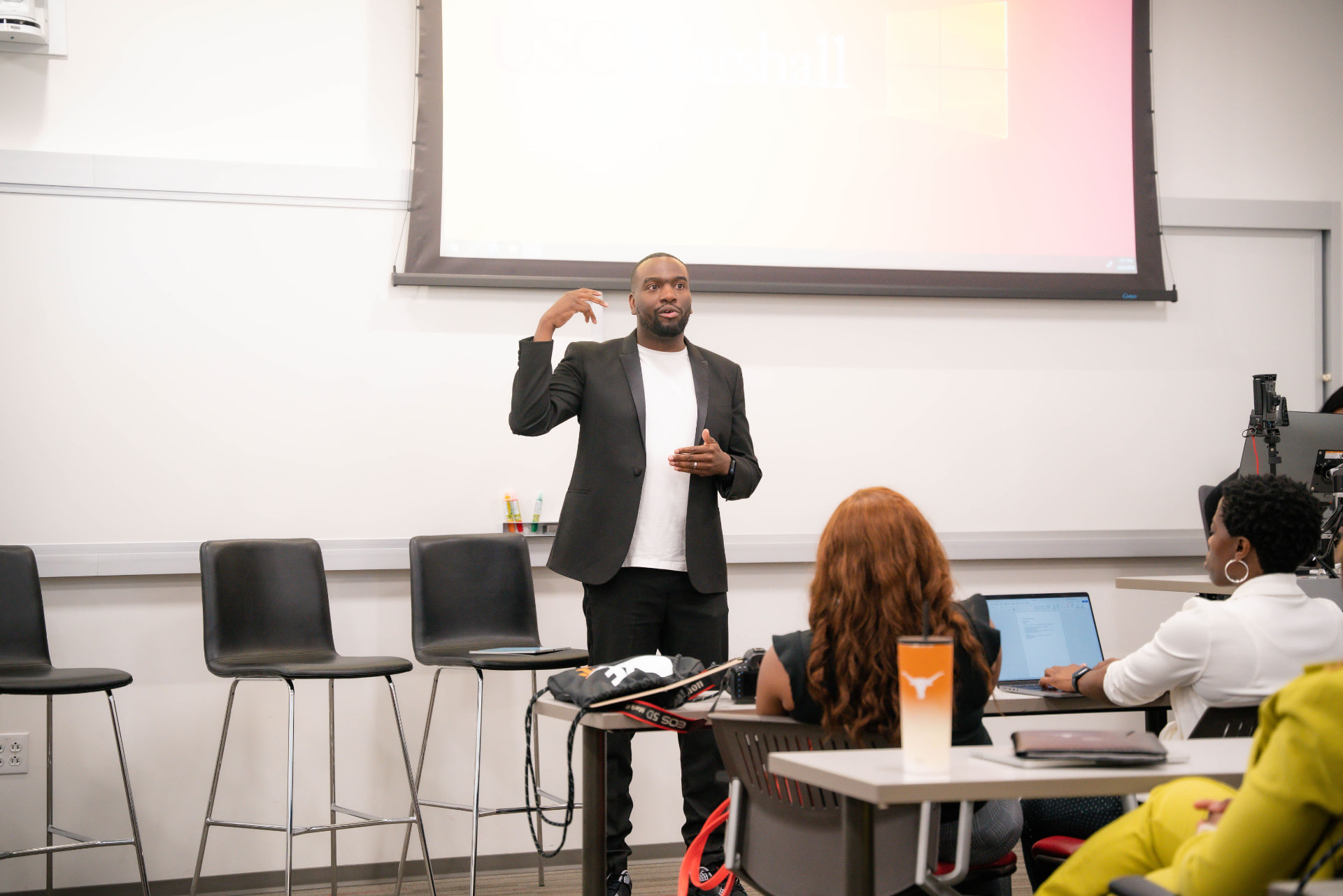 Speaker in a black blazer presenting in front of a USC Marshall projection screen